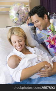 New mother with baby and husband in hospital smiling