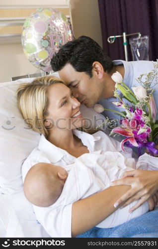 New mother with baby and husband in hospital smiling