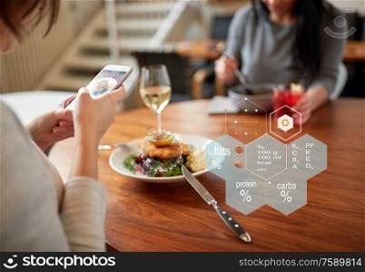 new nordic cuisine, technology and people concept - woman with food on smartphone screen and nutritional value chart r at restaurant. hands with phone and food nutritional value chart