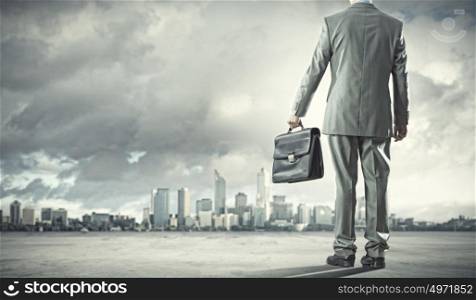 New opportunities. Back view of businessman with suitcase walking on road