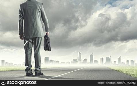 New opportunities. Back view of businessman with suitcase walking on road