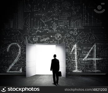 New opportunities. Rear view of businessman entering opened door in black wall