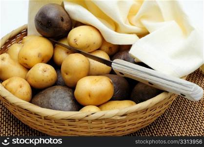 New Potatoes. Small yellow and purple new potatoes in a wicker basket and small paring knife