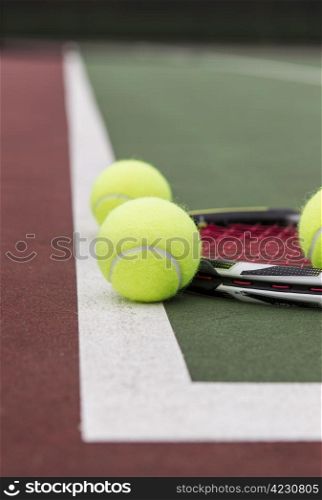 New tennis balls and racket on baseline of court with blurred net in background