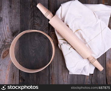 new wooden rolling pin on a textile napkin with embroidery and a round sieve for flour, gray wooden background
