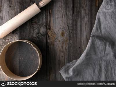 new wooden rolling pin on a textile napkin with embroidery and a round sieve for flour, gray wooden background, copy space