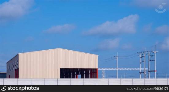 New workshop building with precast concrete fence wall and electric poles in industrial settlement area against blue sky background in panoramic view