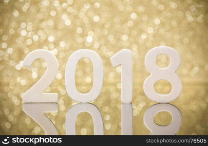 New year 2018 white wood numbers reflexion on glass table in front of glod lights bokeh.