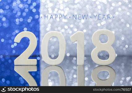New year 2018 white wood numbers reflexion on glass table in front of the blue and silver lights bokeh.