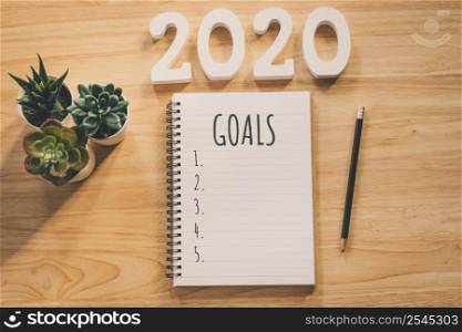 New year 2020 goals list. Office desk table with notebooks and pancil with pot plant.