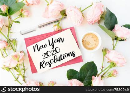 New Year 2020 Resolutions on notebook with coffee and rose flowers, copy space on white background. Top view home office workspace