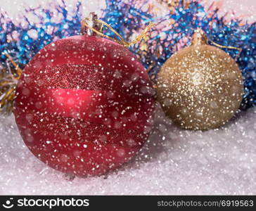New Year background with Christmas balls on snow and background from New Year tree with tinsel and falling snow