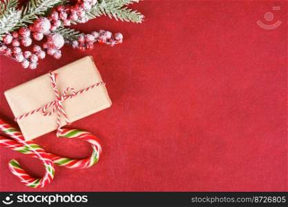New year background with christmas tree branch, candy and gift box on red felt background with space for text. Flat lay, top view.. Christmas background with decorations and gift box on red felt background.