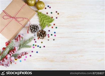 New year background with christmas tree branch, decorative fir tree, fir cones and gift box on white wooden background with space for text. Flat lay, top view.. Christmas background with decorations and gift box on white wooden board