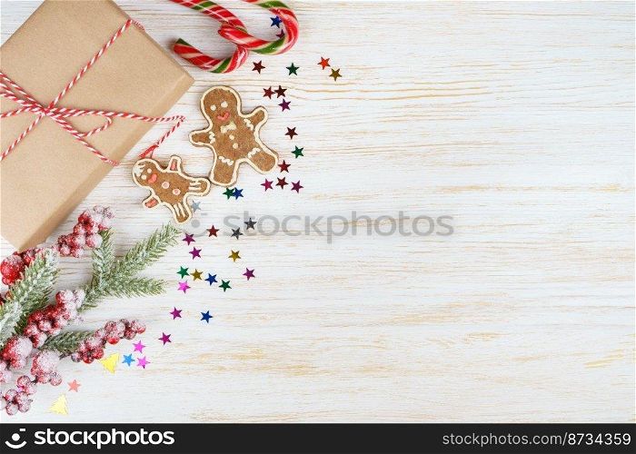 New year background with christmas tree branch, gingerbread man and gift box on white wooden background with copy space. Flat lay, top view.. Christmas background with decorations and gift box on white wooden board