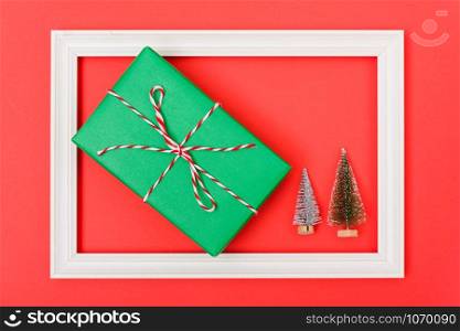 New Year, Christmas Xmas holiday composition, Top view both green fir tree branch and green gift box in frame on red background with copy space