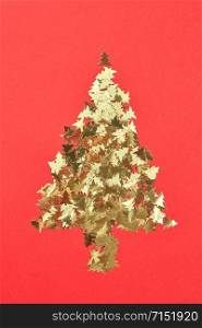 New Year creative decorative tree handmade frome shiny small spruces on a red background with place for text. Greeting holiday card.. Decorative Christmas composition from shiny spruces.