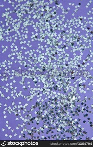 New Year decoration from bright small stars confetti on a lilac background. Holiday creative layout. Top view.. Christmas background from glitter small stars on a lilac paper.