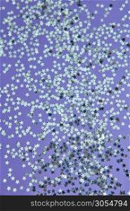 New Year decoration from bright small stars confetti on a lilac background. Holiday creative layout. Top view.. Christmas background from glitter small stars on a lilac paper.