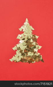 New Year decorative tree handmade from shiny small spruces on a red background, copy space. Greeting holiday card.. Christmas tree handmade from sparkly small spruces.