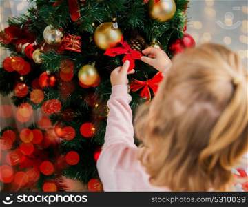 new year, holidays and people concept - close up of little girl decorating christmas tree at home. close up of little girl decorating christmas tree