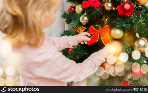 new year, holidays and people concept - close up of little girl decorating christmas tree at home. close up of little girl decorating christmas tree