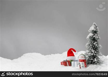 New Year or Christmas card with decor on snow. Toy snowman gifts santa hat and fir tree. Christmas card with decor on snow
