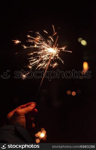 New year party burning sparkler closeup in male hand on unsharp dark background. man holds glowing holiday sparkling hand fireworks
