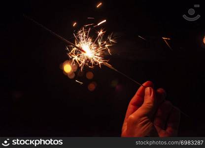 New year party burning sparkler closeup in male hand on unsharp dark background. man holds glowing holiday sparkling hand fireworks
