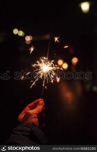 New year party burning sparkler closeup in male hand on unsharp dark background. man holds glowing holiday sparkling hand fireworks