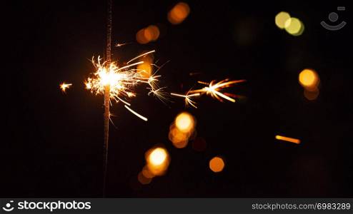 New year party burning sparkler closeup on unsharp dark background. sparkling hand fireworks