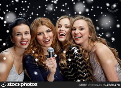 new year party, christmas, winter holidays and people concept - happy women with microphone singing karaoke over black background with snow
