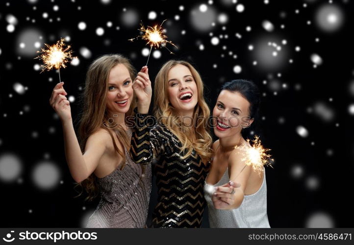 new year party, christmas, winter holidays and people concept - happy young women with sparklers over black background with snow