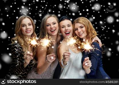new year party, christmas, winter holidays and people concept - happy young women with sparklers over black background with snow