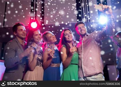 new year party, holidays, technology, nightlife and people concept - smiling friends with glasses of champagne and smartphone taking selfie in club and snow effect
