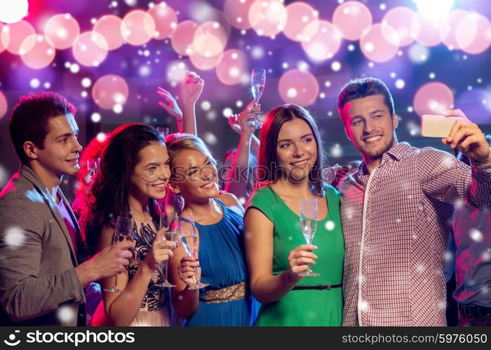 new year party, holidays, technology, nightlife and people concept - smiling friends with glasses of champagne and smartphone taking selfie in club and snow effect