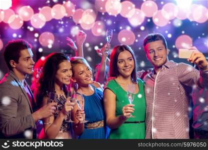 new year party, holidays, technology, nightlife and people concept - smiling friends with glasses of champagne and smartphone taking selfie in club and snow effect