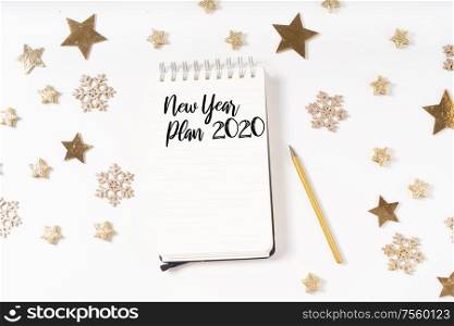 New Year Plan for Cristmas and 2020 New Year. Holiday decorations and ruled notebook with wish list on white desk, flat lay. Christmas flat lay scene with golden decorations