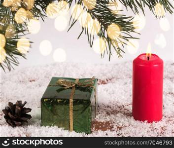 New Year&rsquo;s background - a candle and a green box on the snow under the spruce branches