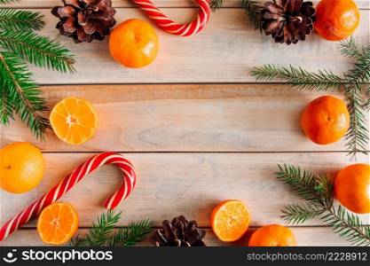New Year’s decor. Christmas tree branches, pine cones, tangerines and candies on a wooden background.. New Year’s decor. Christmas tree branches, pine cones, tangerines and candies on wooden background.