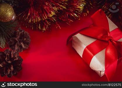 New Year’s gift with a red ribbon in craft brown paper. Christmas composition of cones, tinsel and gifts on a red background.