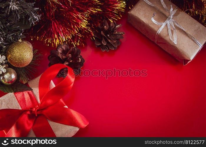New Year’s gift with a red ribbon in craft brown paper. Christmas composition of cones, tinsel and gifts on a red background.