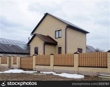 New yellow brick cottage behind a high fence in early spring