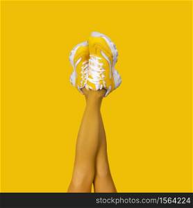 New Yellow female sneakers on long slender woman legs in yellow tights isolated on yellow background. Monochrome pop art concept. Square composition. New Yellow female sneakers on long slender woman legs in yellow tights isolated on yellow background.