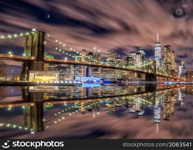 New york skyline from Brooklyn bridge in blue hour with moon present and reflection on Hudson river