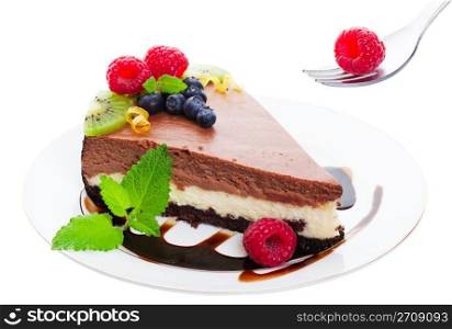 New York Style, triple layer, chocolate cheesecake served on a chocolate drizzled plate and garnished with raspberries, blueberries, kiwi, and fresh sprigs of lemon balm. Delicate citrus curls add a touch of elegance. Shot on white background.
