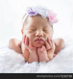 Newborn 7 day old baby girl on his white bed relaxing and flower on her head