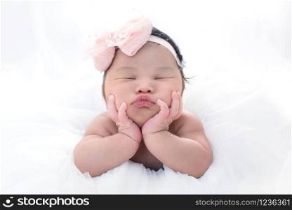 Newborn 7 day old baby girl on his white bed relaxing and pink ribbon bow on her head