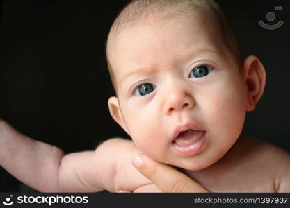 Newborn baby against black background with big eyes looking into the camera being held by her mother