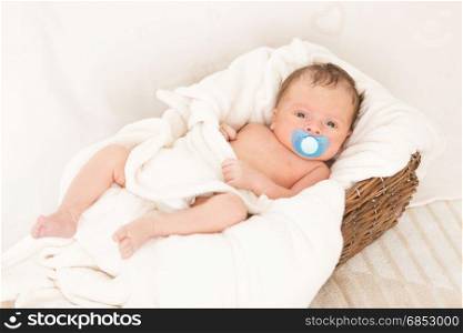 Newborn baby boy lying in old wicker basket covered by blanket